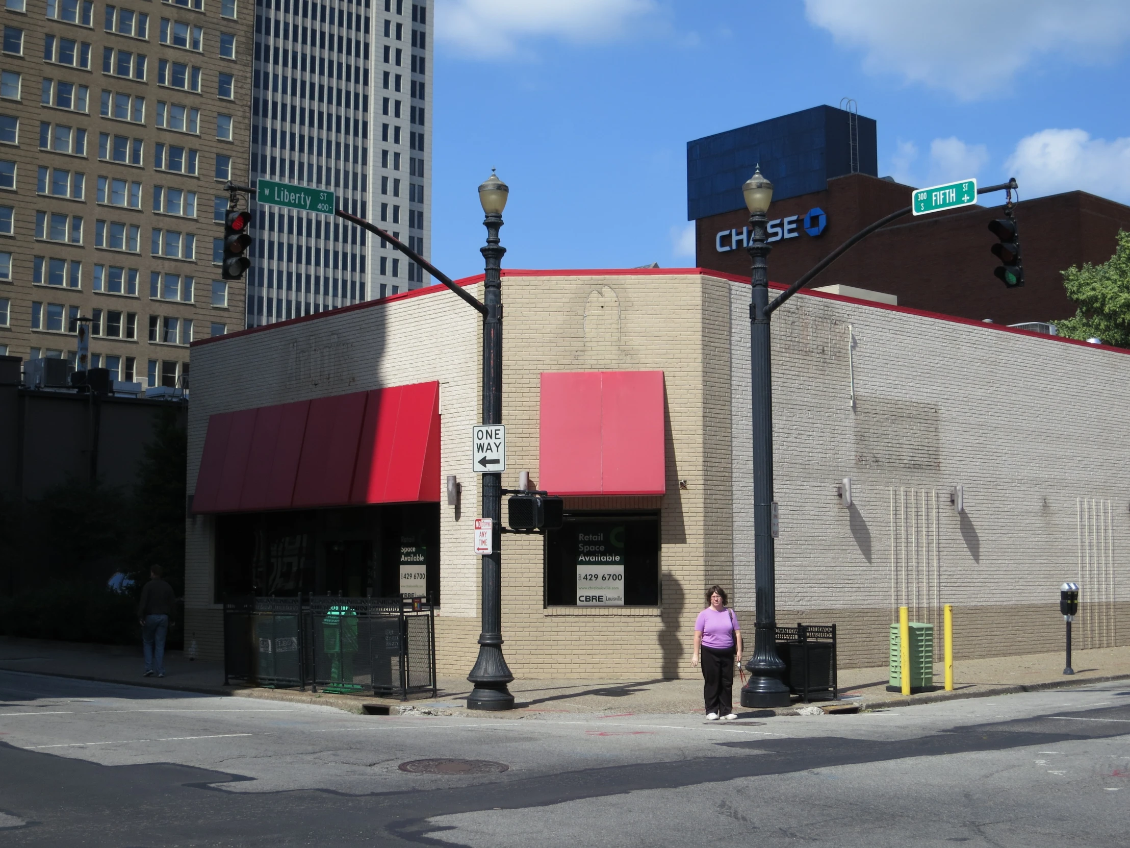 woman standing by street corner in front of building with red awning