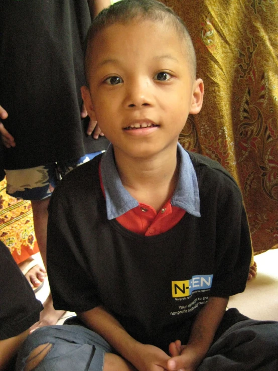 a boy with black shirt and red tie sitting next to a pillow