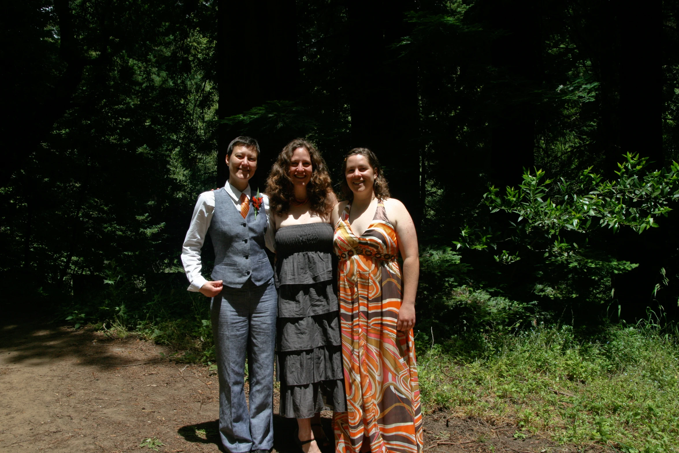 four women standing around each other in front of trees