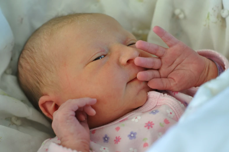 a close up of a baby laying in bed with its hand on her face