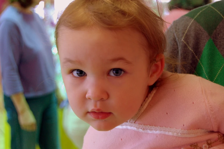 a little girl with a sweater on is staring straight ahead