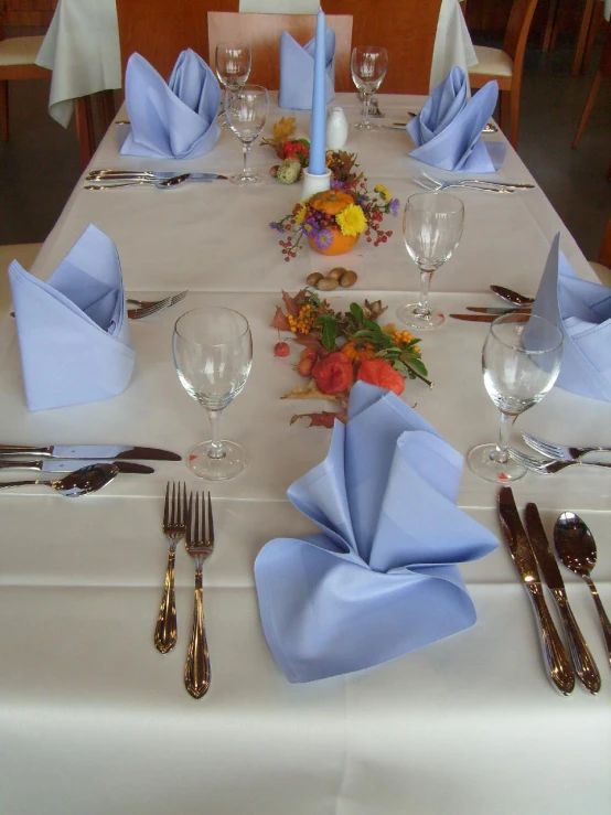 a white table with blue napkins and silver ware