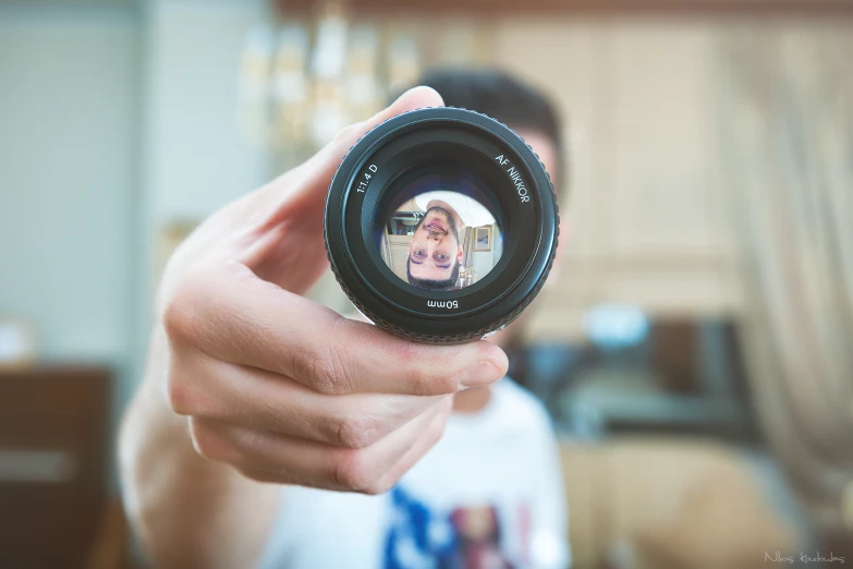 a man holding a camera lens with a woman's reflection in it