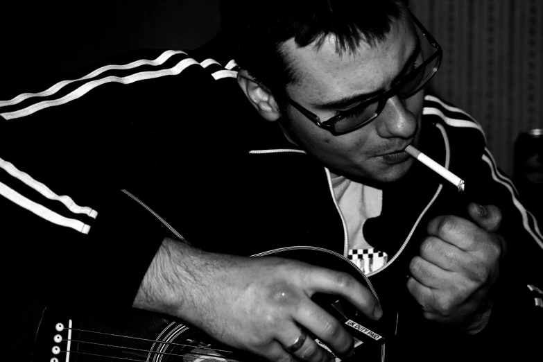 a man playing guitar while holding a cigarette