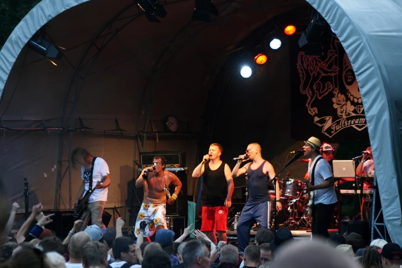 a group of men singing on stage with a large crowd watching