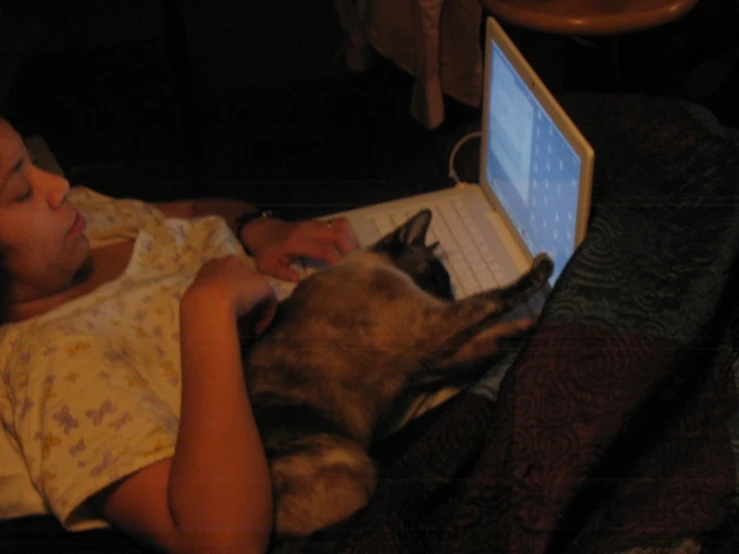 a girl laying in bed with a dog and a laptop