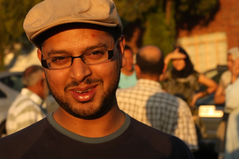 man wearing glasses and hat smiling while standing near people