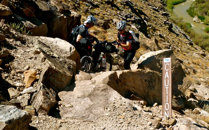 three mountain bikers sit on rocks on a trail