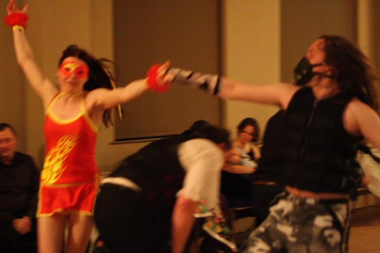 two woman with red painted face paint dancing and others sitting in the background