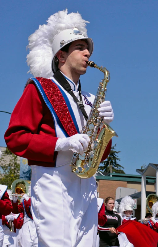 the man is wearing a long red jacket and white costume and playing his saxophone