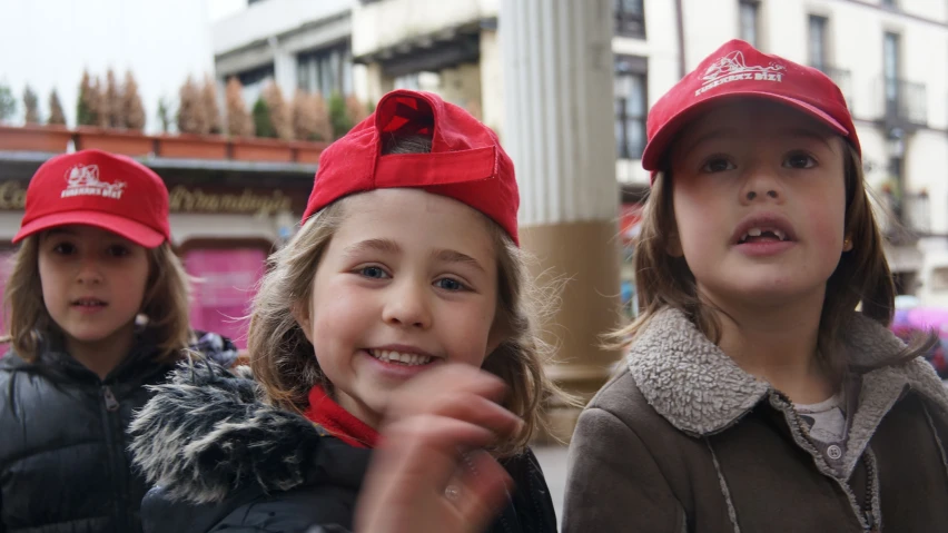 two young children wearing red caps eating on the street