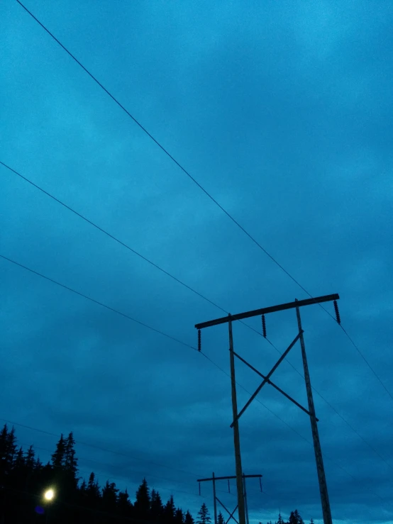 an electric pole standing next to power lines and trees at dusk