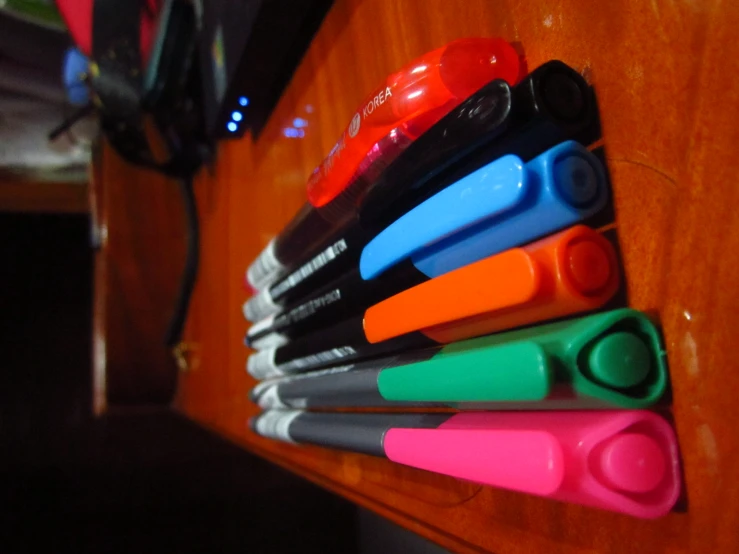 various colored pens sit on the edge of a wooden table