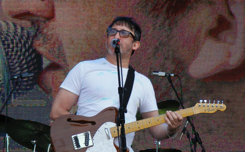 a male with glasses and white shirt playing a guitar