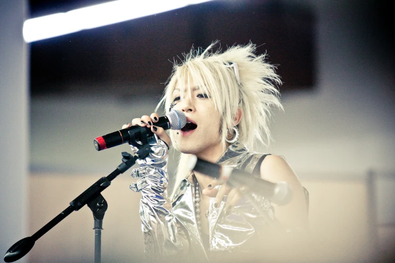 an asian woman in a silver top sings into a microphone