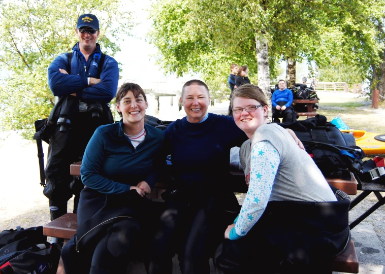 people smiling while sitting on wooden benches near water