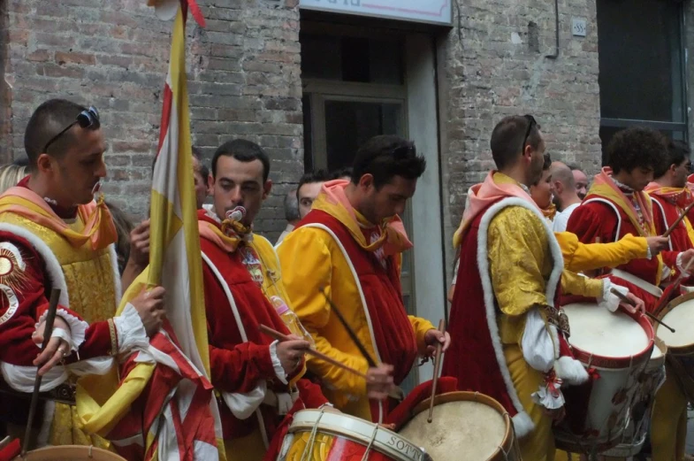 men in traditional costumes play with drums in front of the building