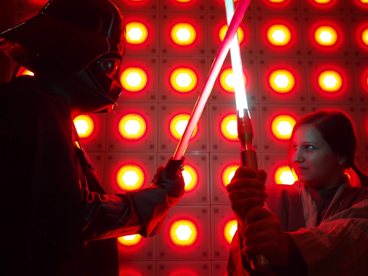 two people in star wars costume holding lights and a sword