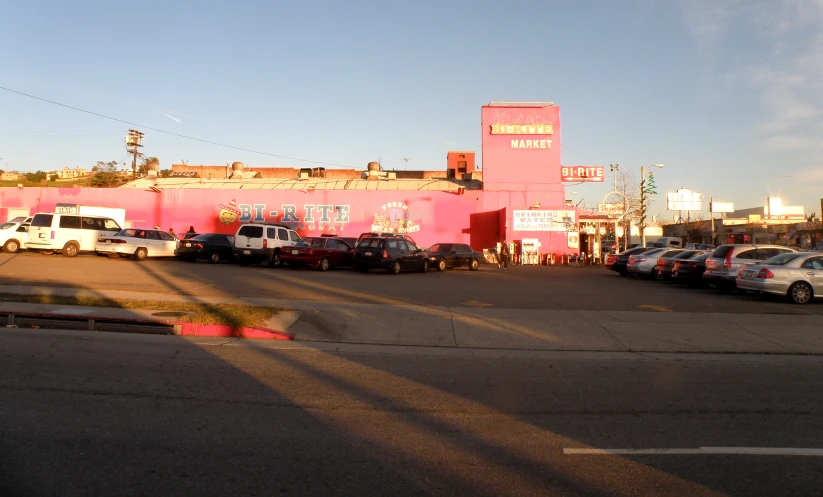 the large building is painted pink and has many cars parked outside