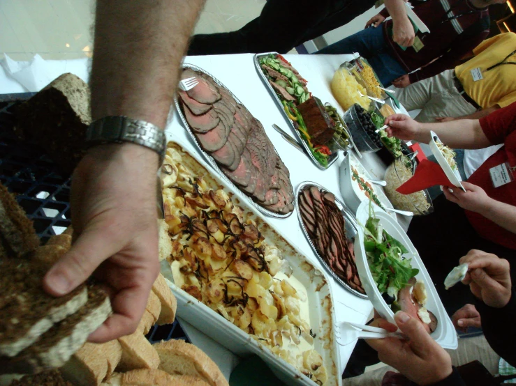 the crowd is getting food from a table of sandwiches