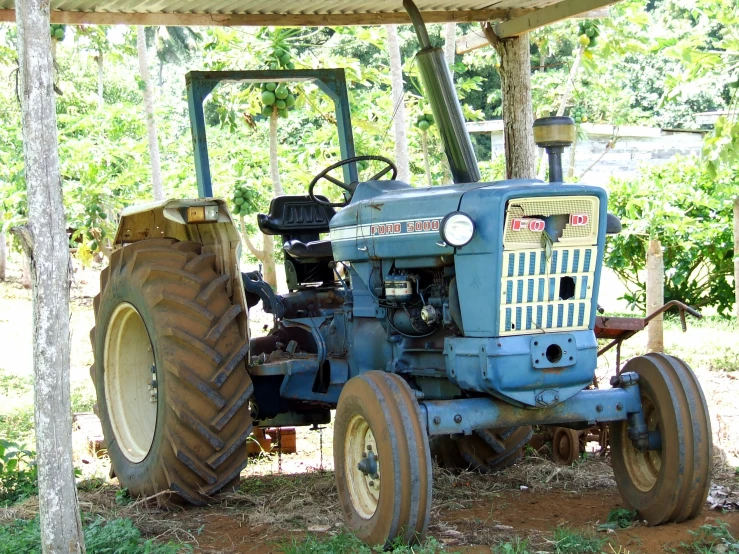 a blue tractor parked under a wooden structure