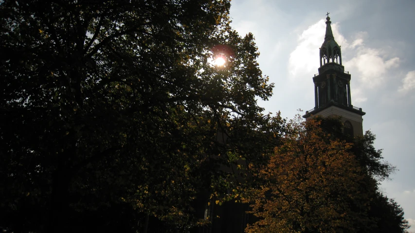 a clock tower above trees with the sun shining through the clouds