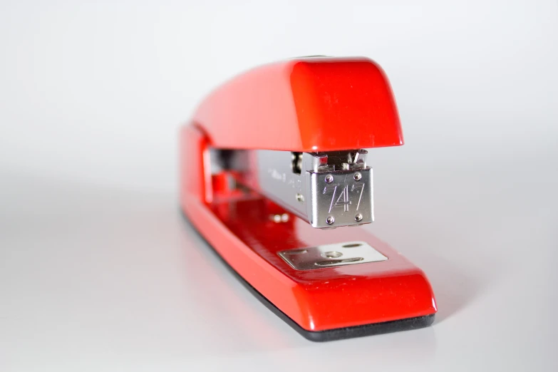 there is a red metal stapler on a table