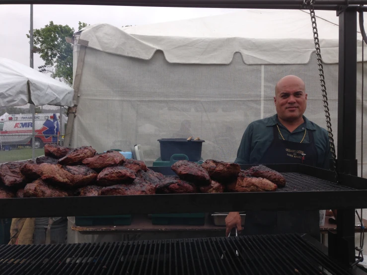 man in green shirt and apron with barbecues outside