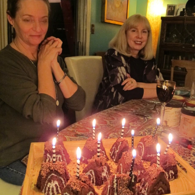 two women sitting at a table with a large cake with candles on it