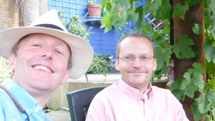 two men smiling at camera with green plants on either side