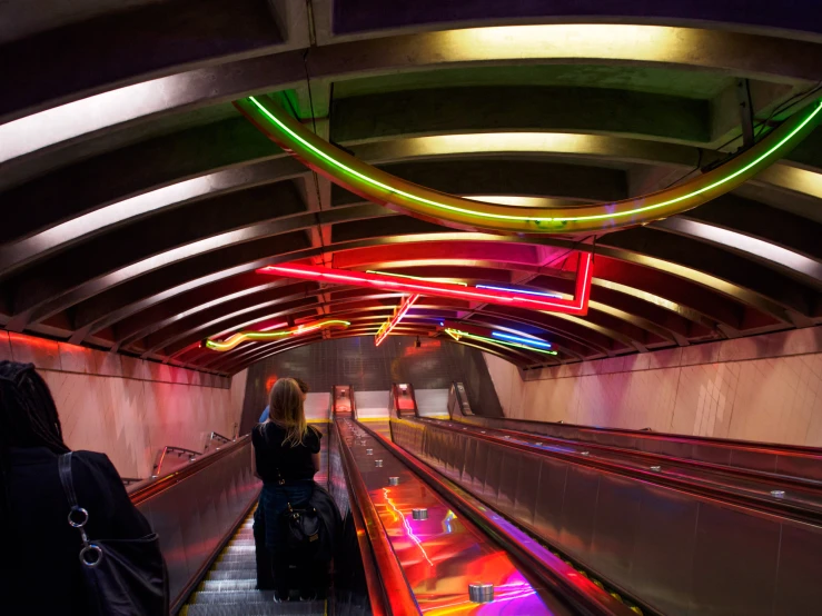 a woman riding an escalator down a brightly lit walkway