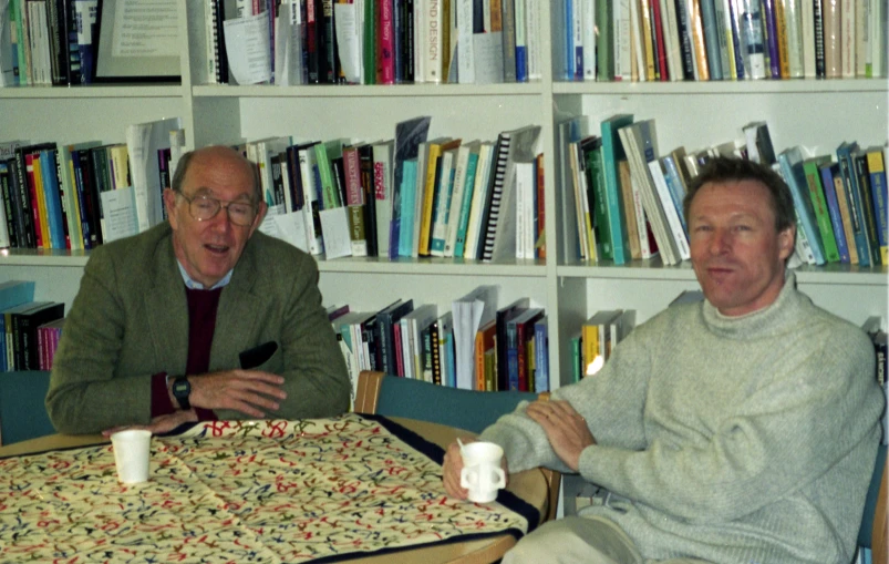 two older men are sitting at a table with cups