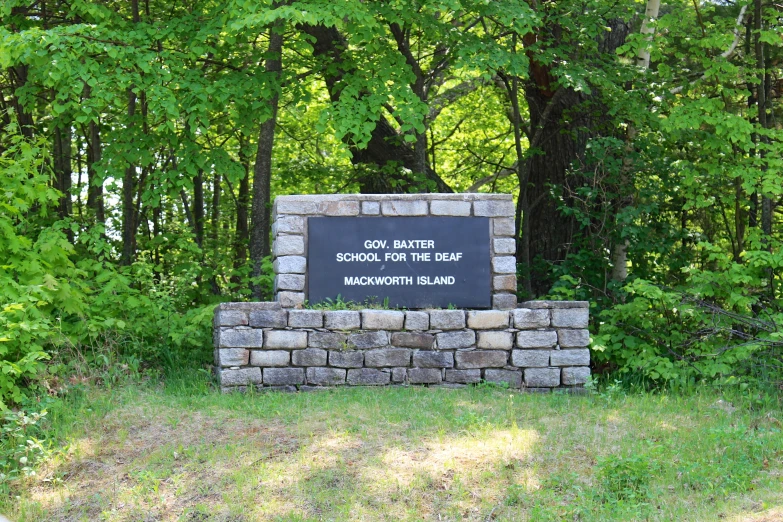 a welcome sign with stones and a brick column sits in the grass