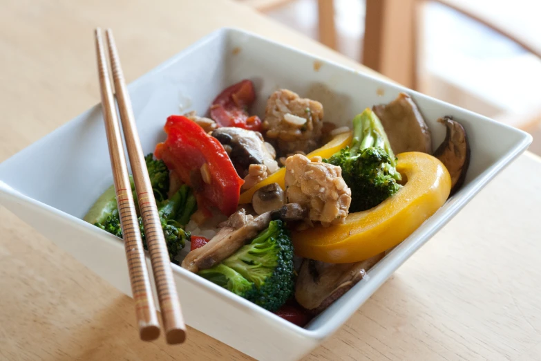 a square white dish of meat and vegetables with chop sticks