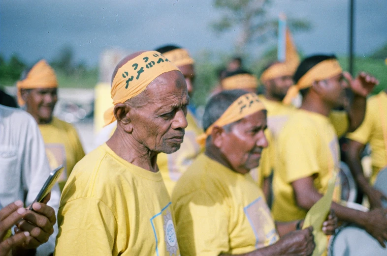 men with yellow colored head coverings wait in line