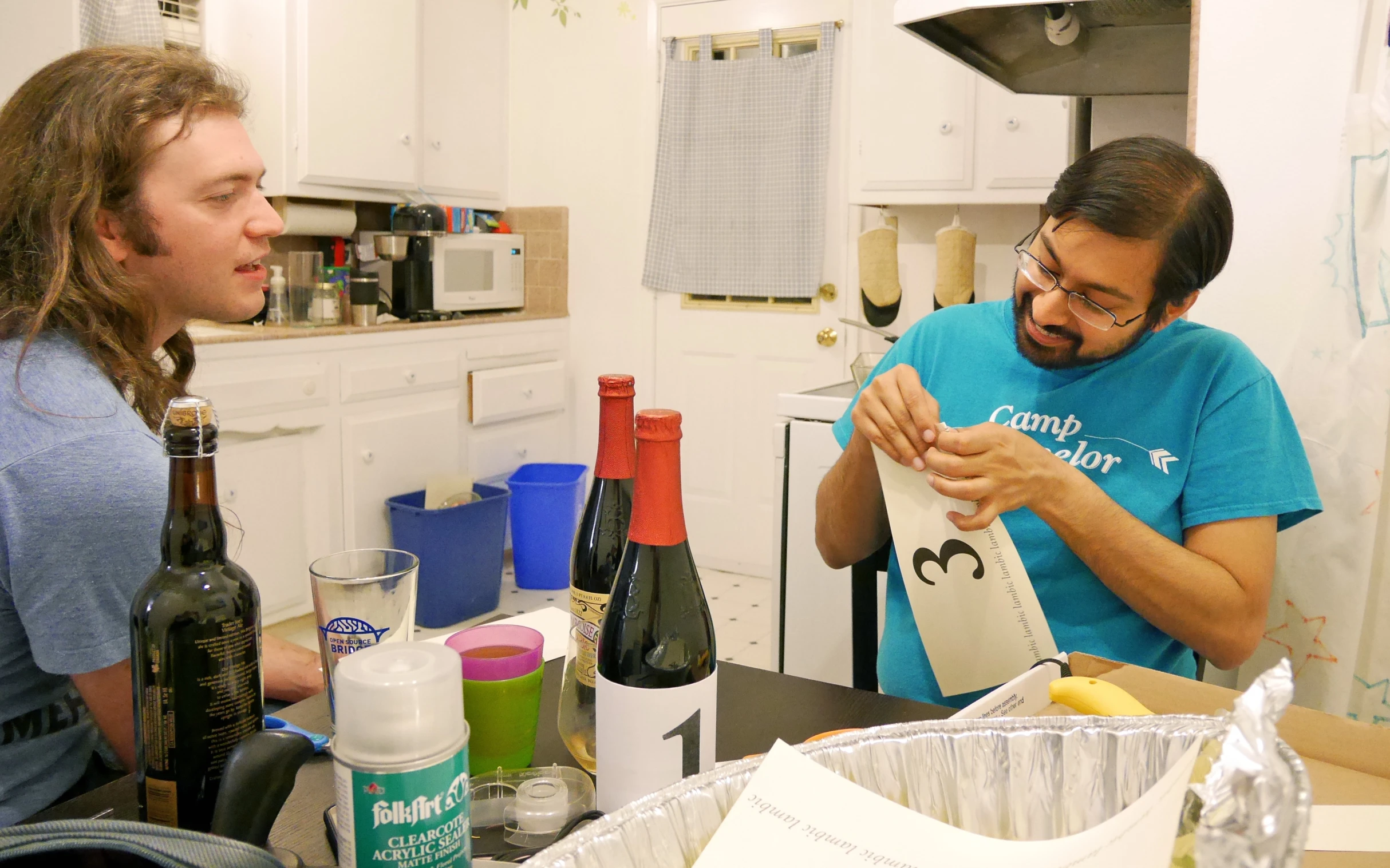 two men standing in the kitchen looking at a paper bag