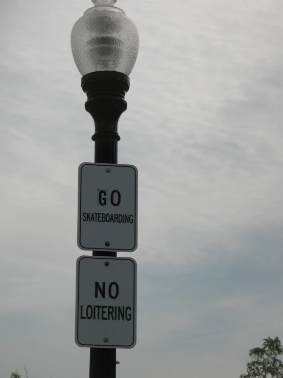there are two street signs that include no loitering and go skateboarding