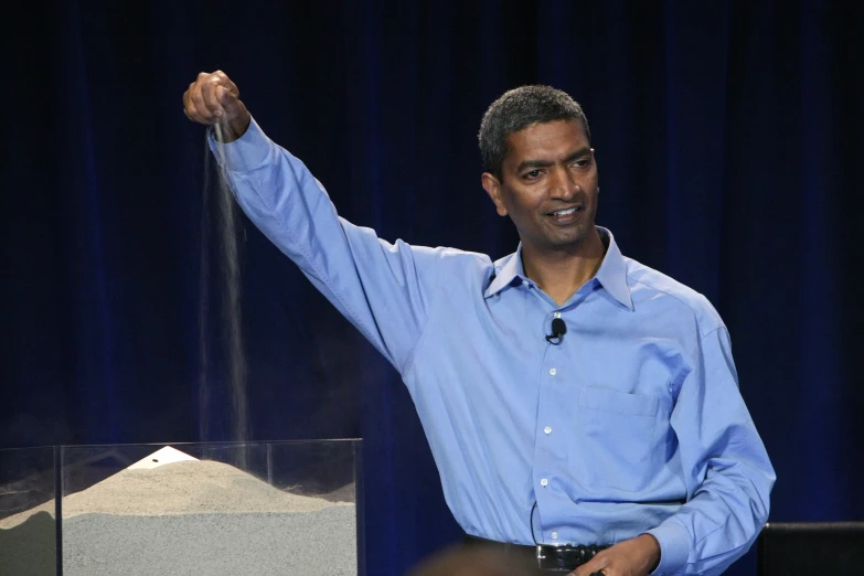 man in blue shirt speaking at podium with arm raised