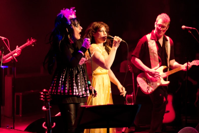 three women on stage singing and playing music