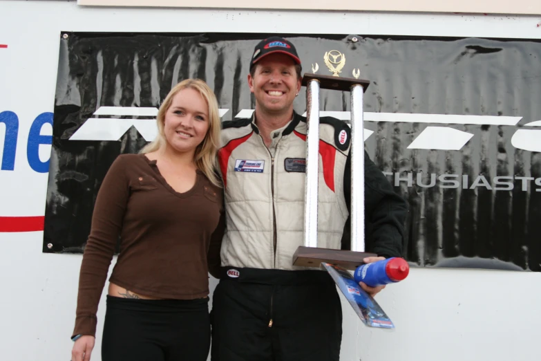 two people stand side by side holding trophies