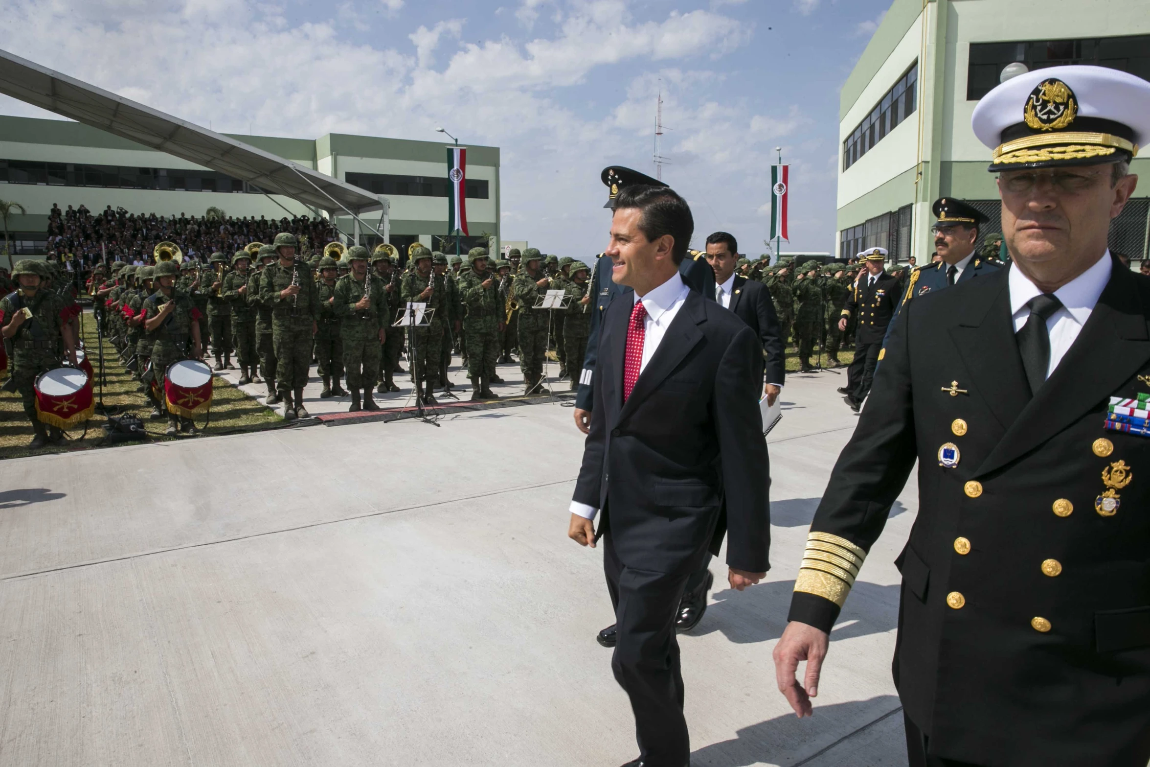 two military men wearing suits and ties walk past other uniformed men in uniforms