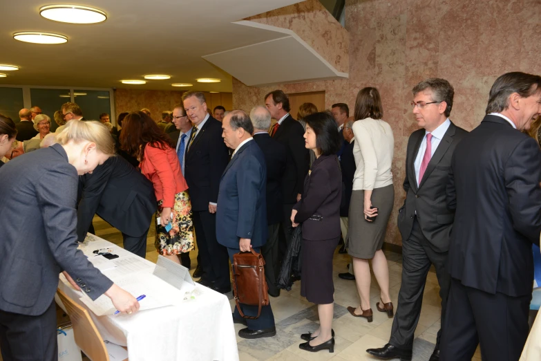 many people in suits and ties standing around tables with papers