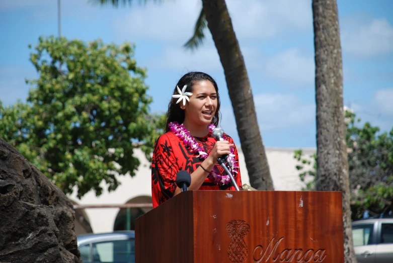 a woman speaks at a podium next to a palm tree