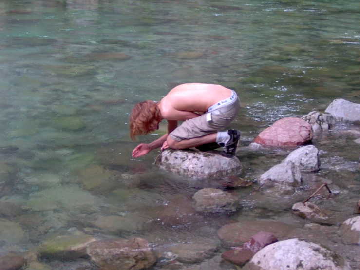 the boy is standing on a rock and playing with the water