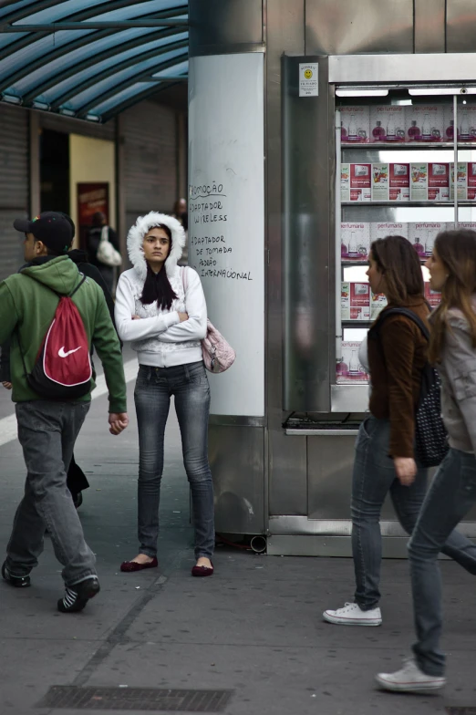 four people waiting at a bus stop and one is wearing a hat