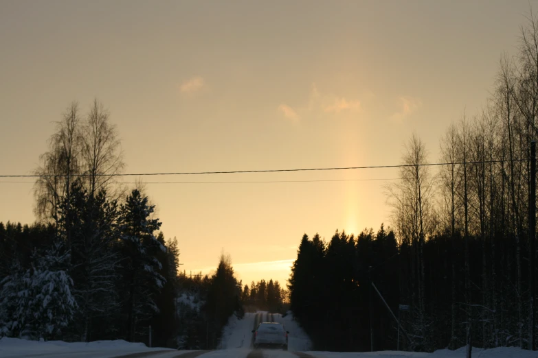 a road with snow on the ground and sun setting in background