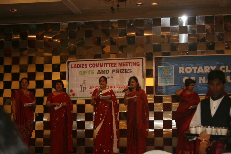 women dressed in red dresses are singing in front of a group