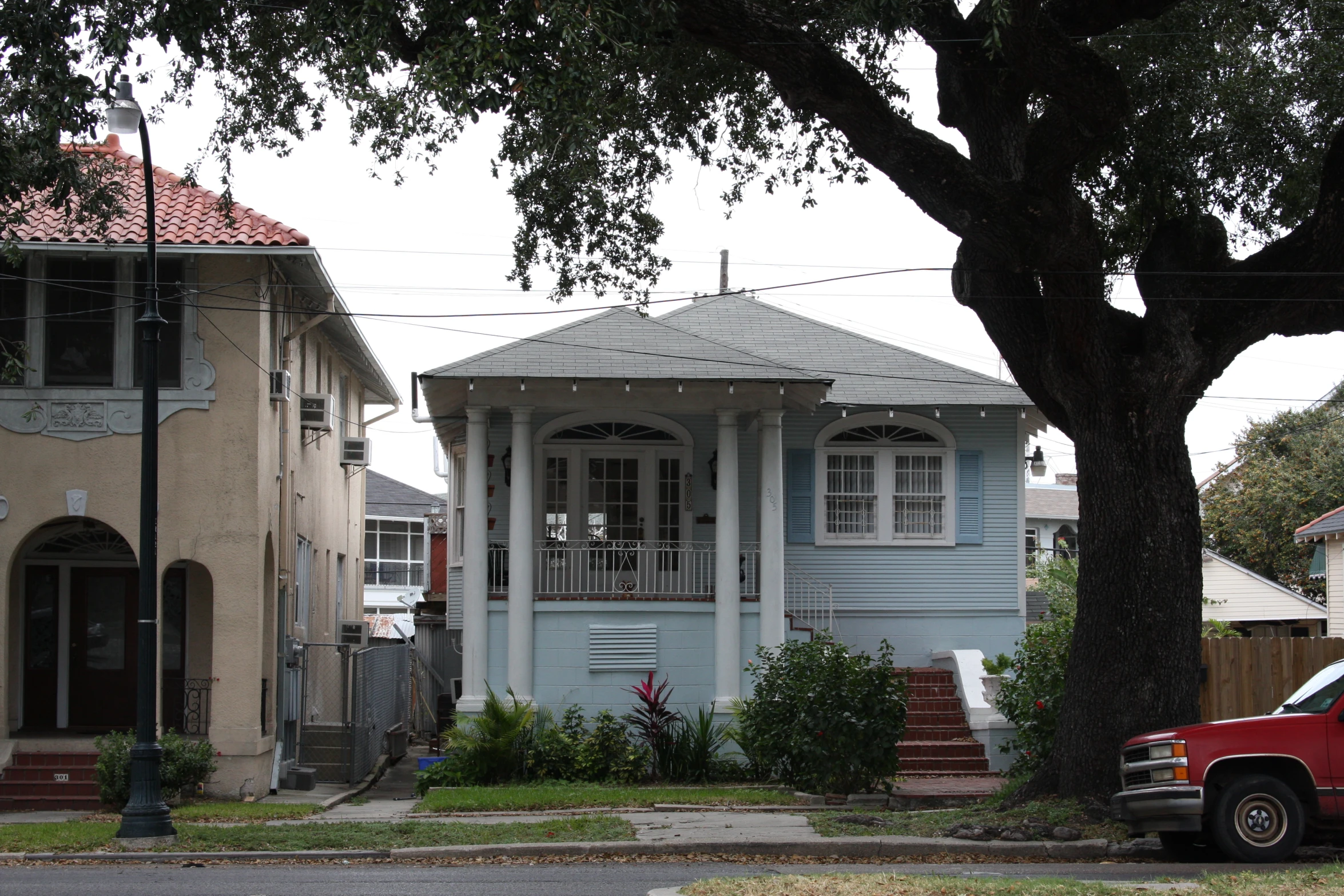 the blue house with white trim is next to trees and cars