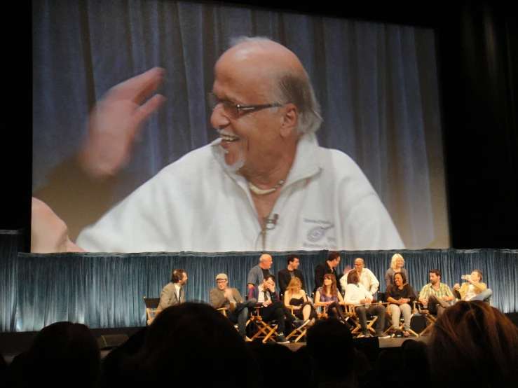 people in front of a large screen with the image of an older man laughing