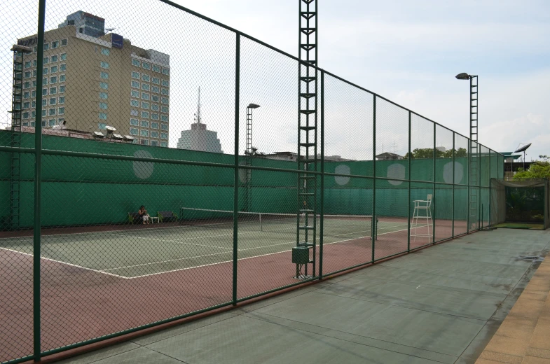 an asphalt tennis court next to green fence